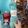 Turquoise yarn skein held in a hand with a blurred store background