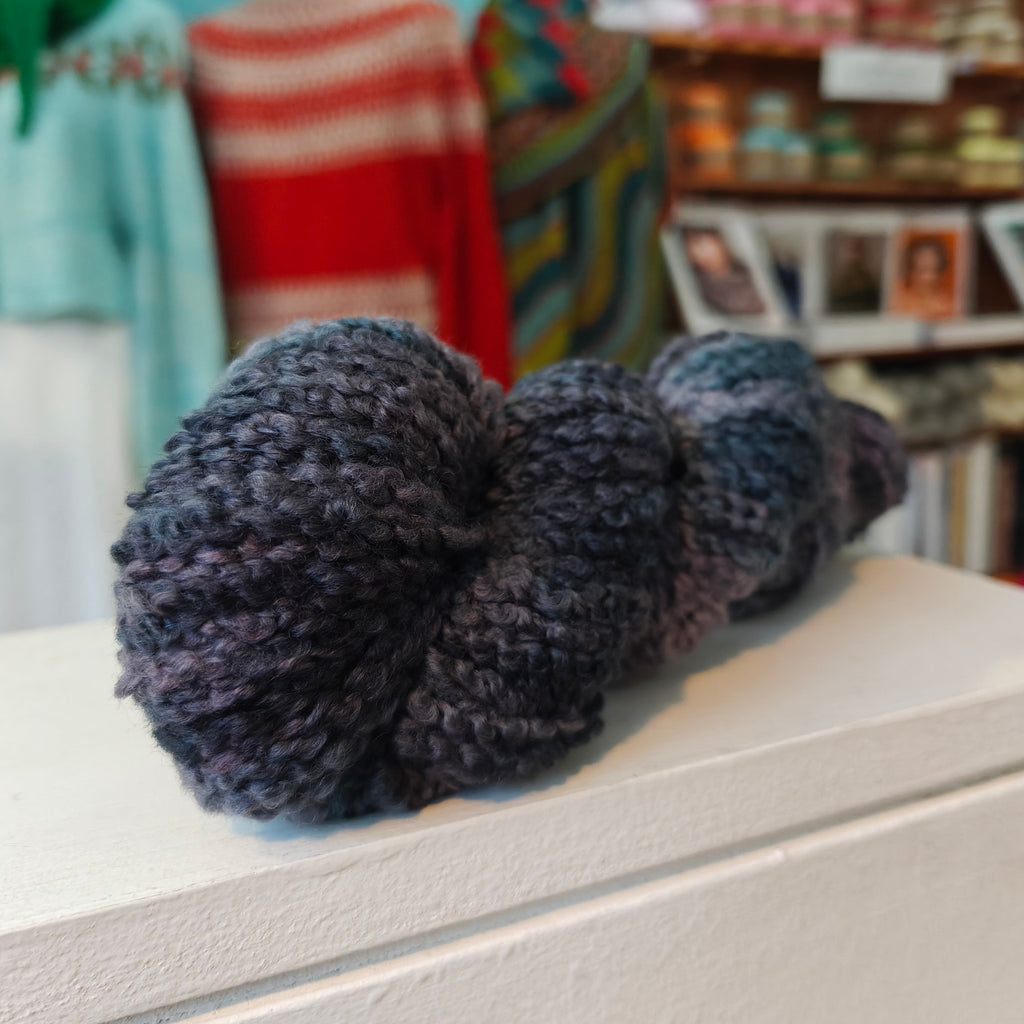 skein of black teal yarn on a white wooden shelf