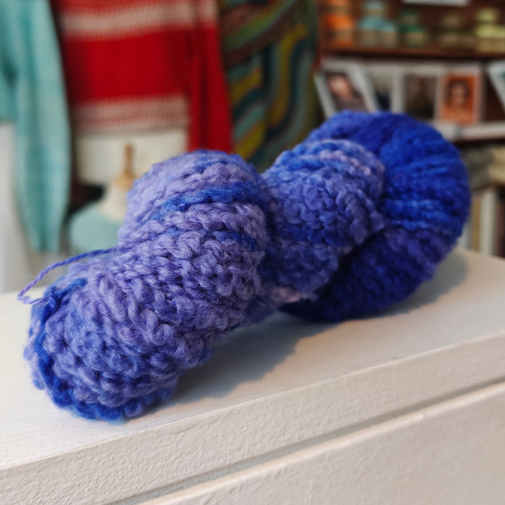 blue purple skein of yarn on a surface with a blurred indoor background