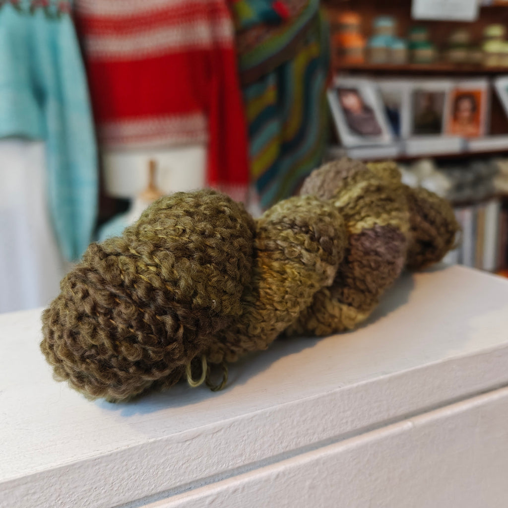 one skein of yarn in green, brown, and beige on a surface with a blurred background.