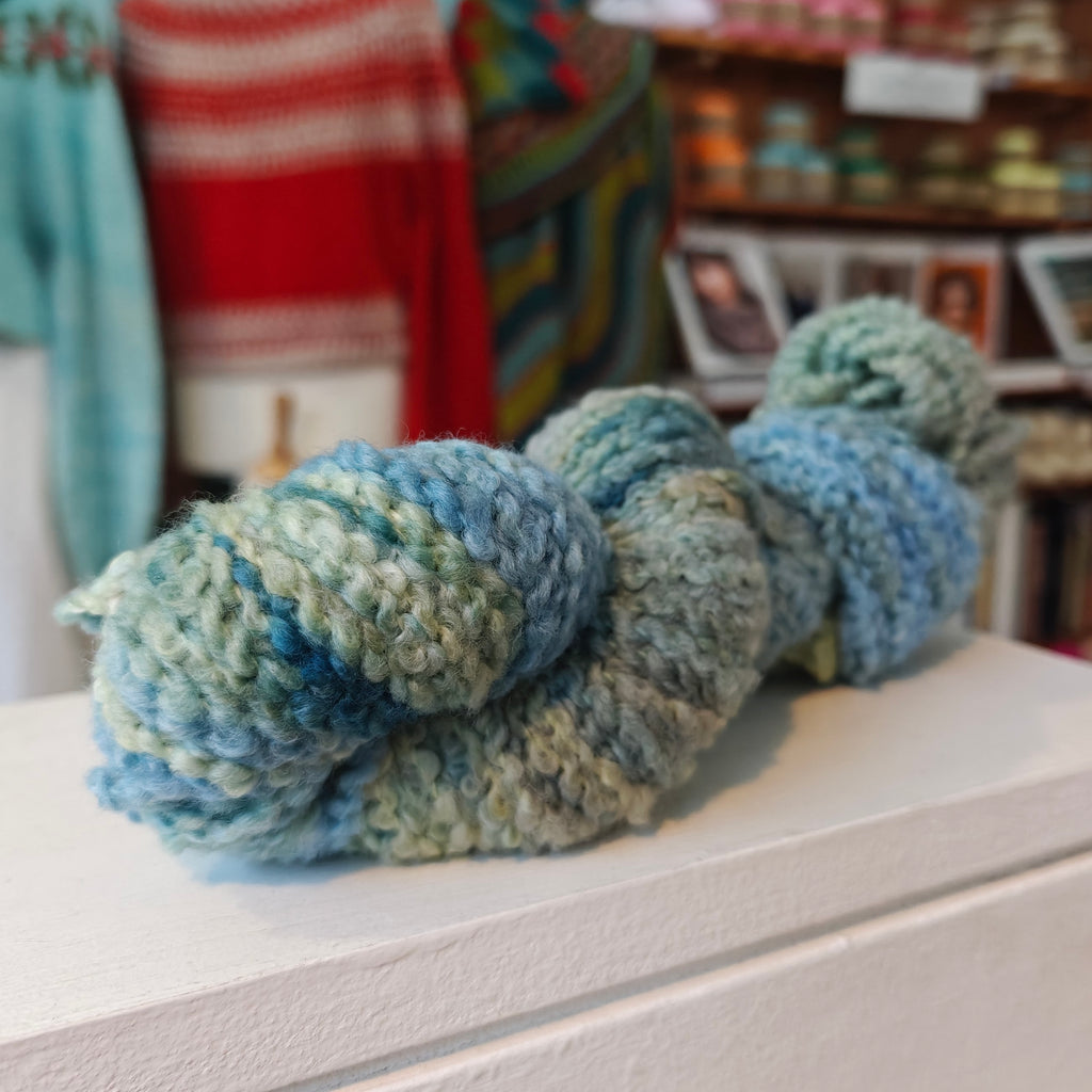 Blue and green yarn skein on a surface with a blurred background