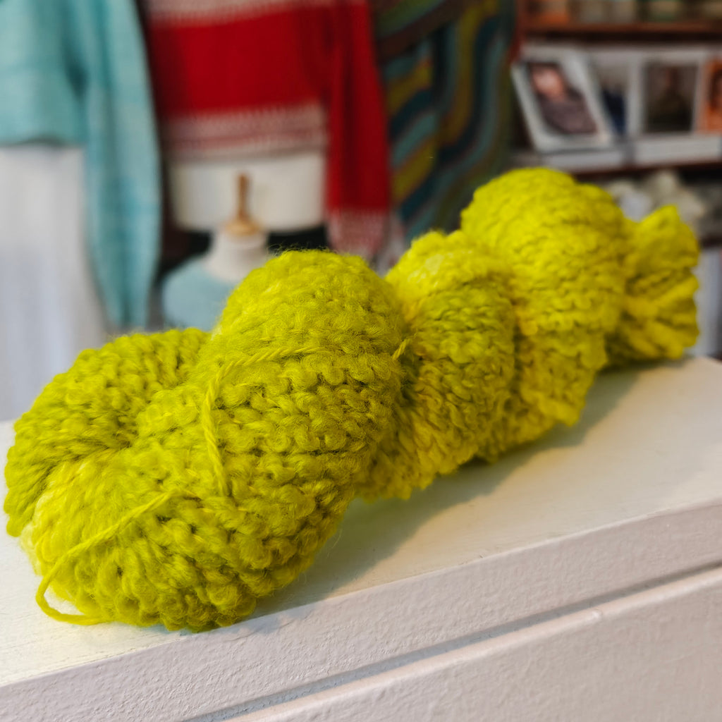 skein of bright green yarn on a shelf with a blurred indoor background