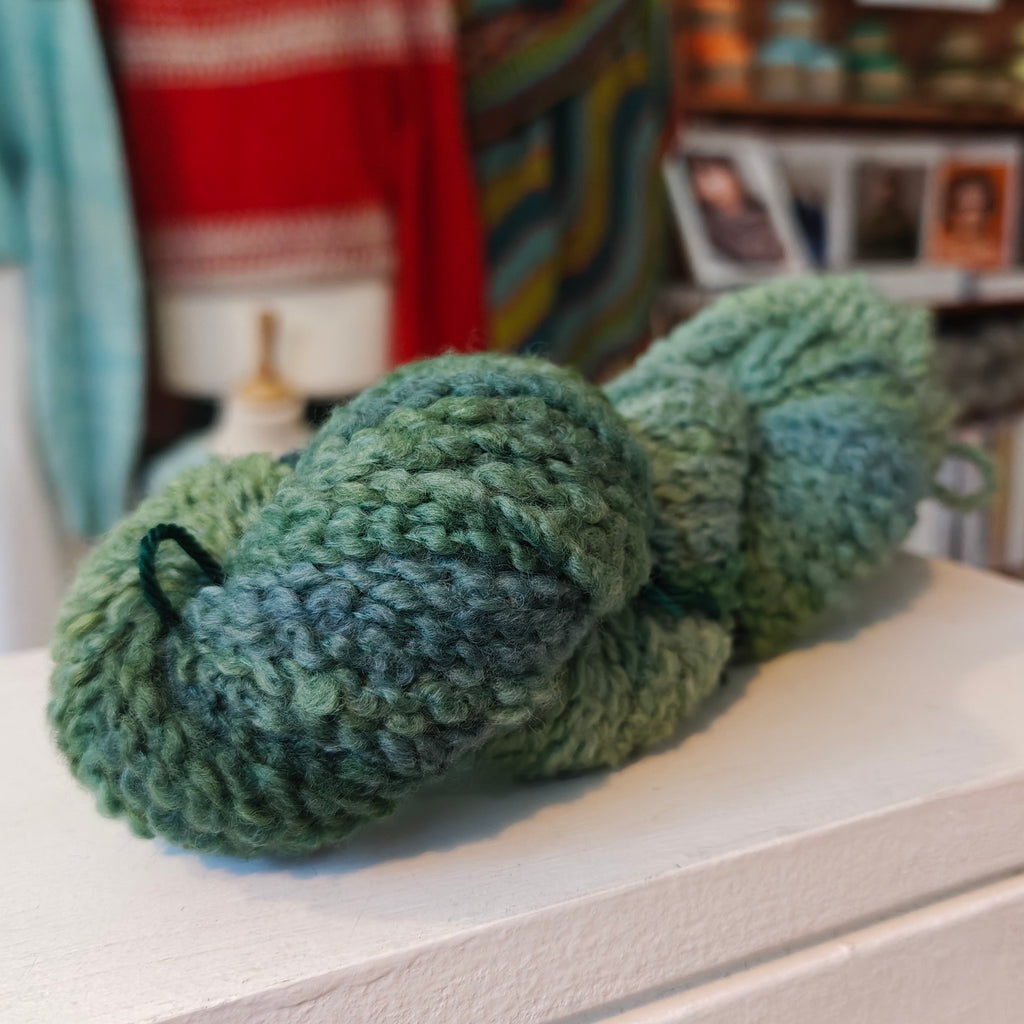 one skein of green yarn on a surface with a blurred background