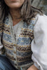A close-up of a person wearing a cream-colored knit button-front vest with blue, brown, and mustard geometric patterns, layered over a white shirt.