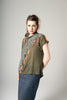 Woman wearing a green top with decorative shoulder pieces against a plain background