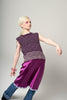 Person wearing a sleeveless purple top and skirt with blue jeans on a gray background