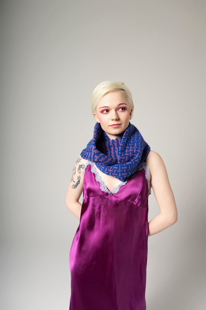 Woman wearing a purple dress and blue patterned scarf against a gray background