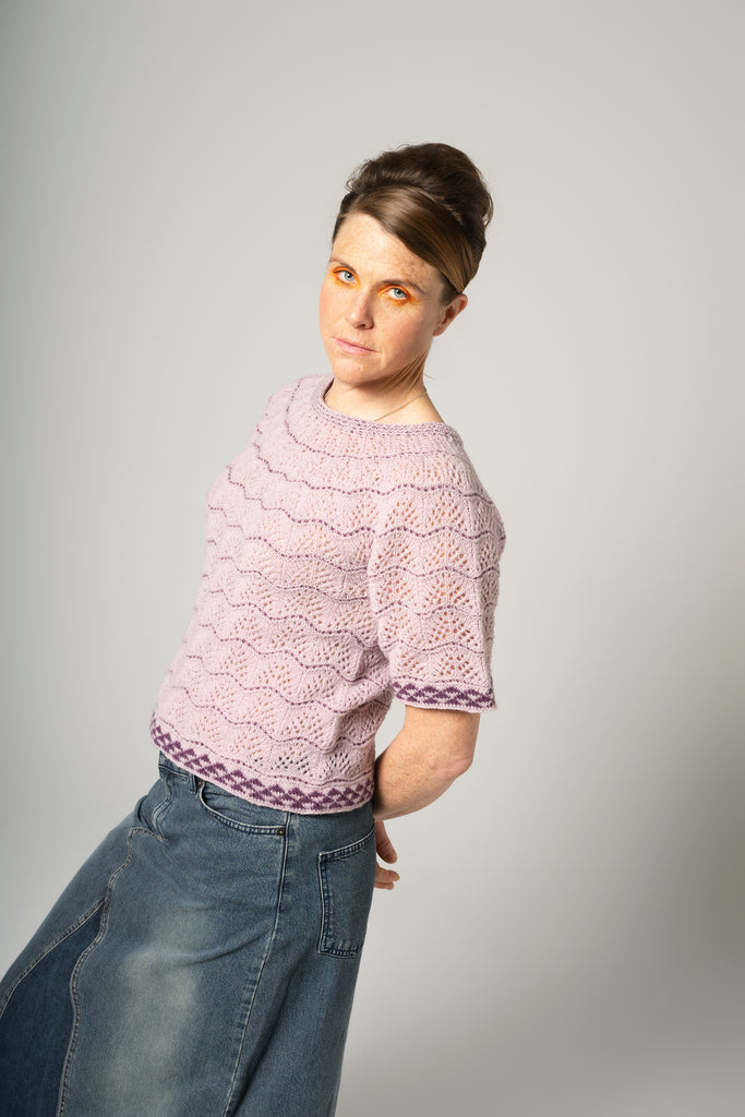 Person wearing a pink patterned shirt and blue jeans on a gray background
