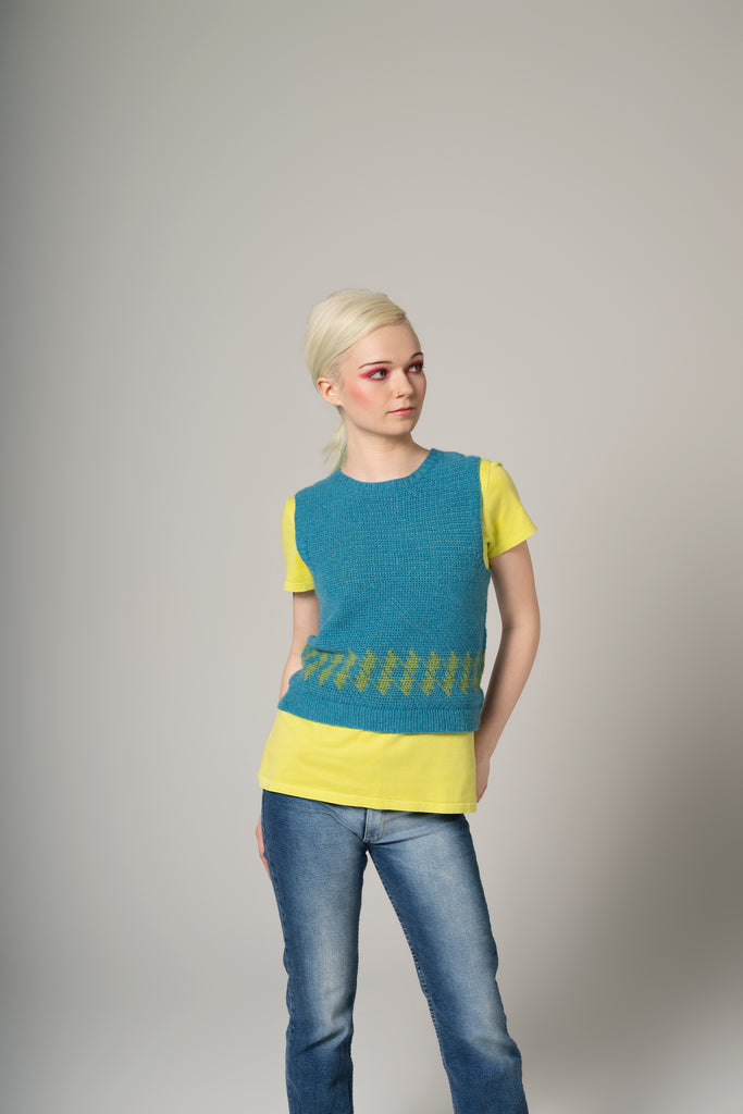 Woman wearing a blue and yellow sleeveless top with jeans on a gray background