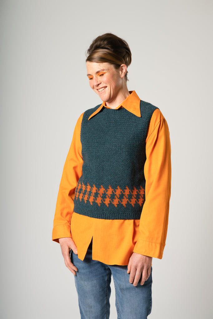 Person wearing an orange shirt over a patterned vest on a plain background