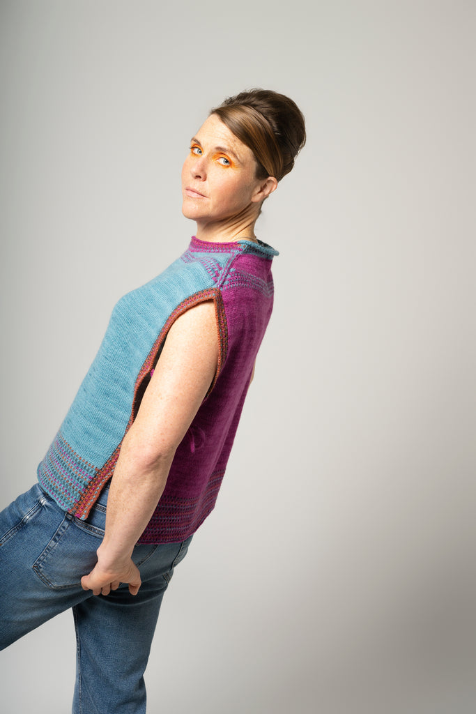 Person wearing a two-tone sleeveless sweater with blue and purple colors on a plain background