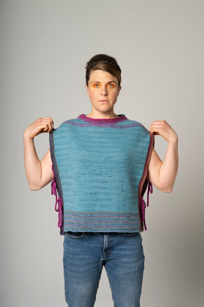 Person wearing a blue knitted vest with purple accents on a gray background