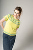 Woman wearing a yellow patterned shirt and blue jeans against a gray background