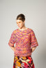 Woman wearing a colorful knitted sweater and patterned skirt against a plain background