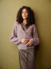Woman wearing a light purple cardigan over a brown top and pants against a green background