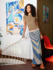 Woman wearing a long, patterned skirt standing in a room with colorful artwork on the walls.