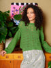 Woman wearing a green sweater standing in front of a decorative wall piece.