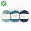 Three skeins of BC Garn Hamelton Tweed yarn in blue, green, and navy colors, indicating the product is organic and suitable for knitting and crochet.