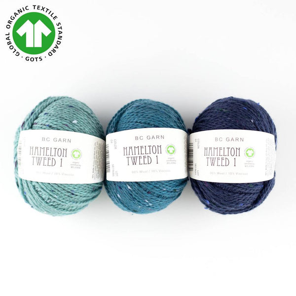Three skeins of BC Garn Hamelton Tweed yarn in blue, green, and navy colors, indicating the product is organic and suitable for knitting and crochet.