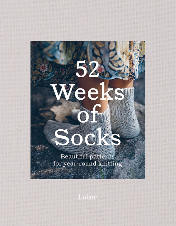 The cover of the book '52 Weeks of Socks' by Laine, showing a pair of knitted socks against a rustic background.