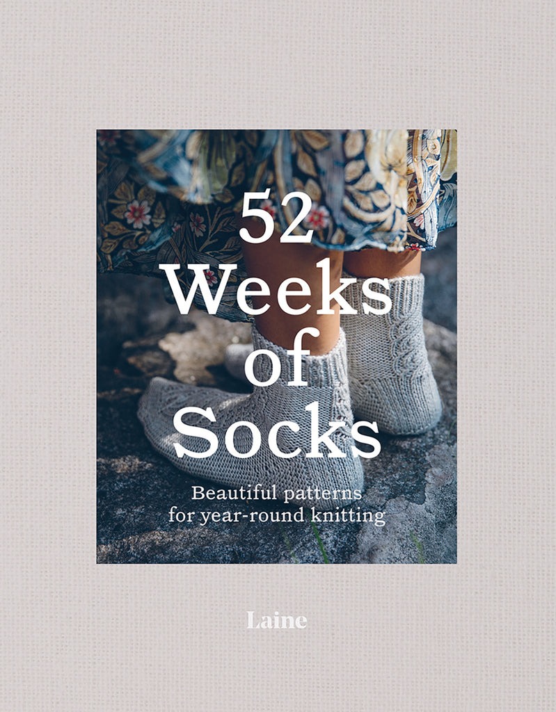 The cover of the book '52 Weeks of Socks' by Laine, showing a pair of knitted socks against a rustic background.